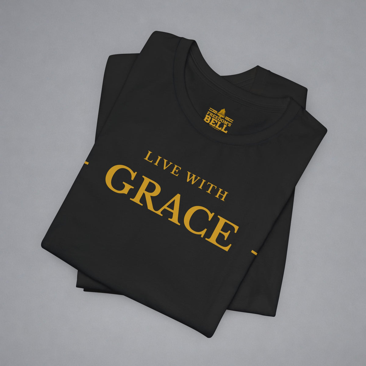 A folded black t-shirt with gold text reading 'LIVE WITH GRACE' and a gold 'BELL' logo printed inside the collar, displayed on a neutral gray background.