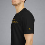 A man wearing a black short-sleeve t-shirt with gold text on the chest and a small gold logo on the sleeve, shown in a side profile against a gray background.
