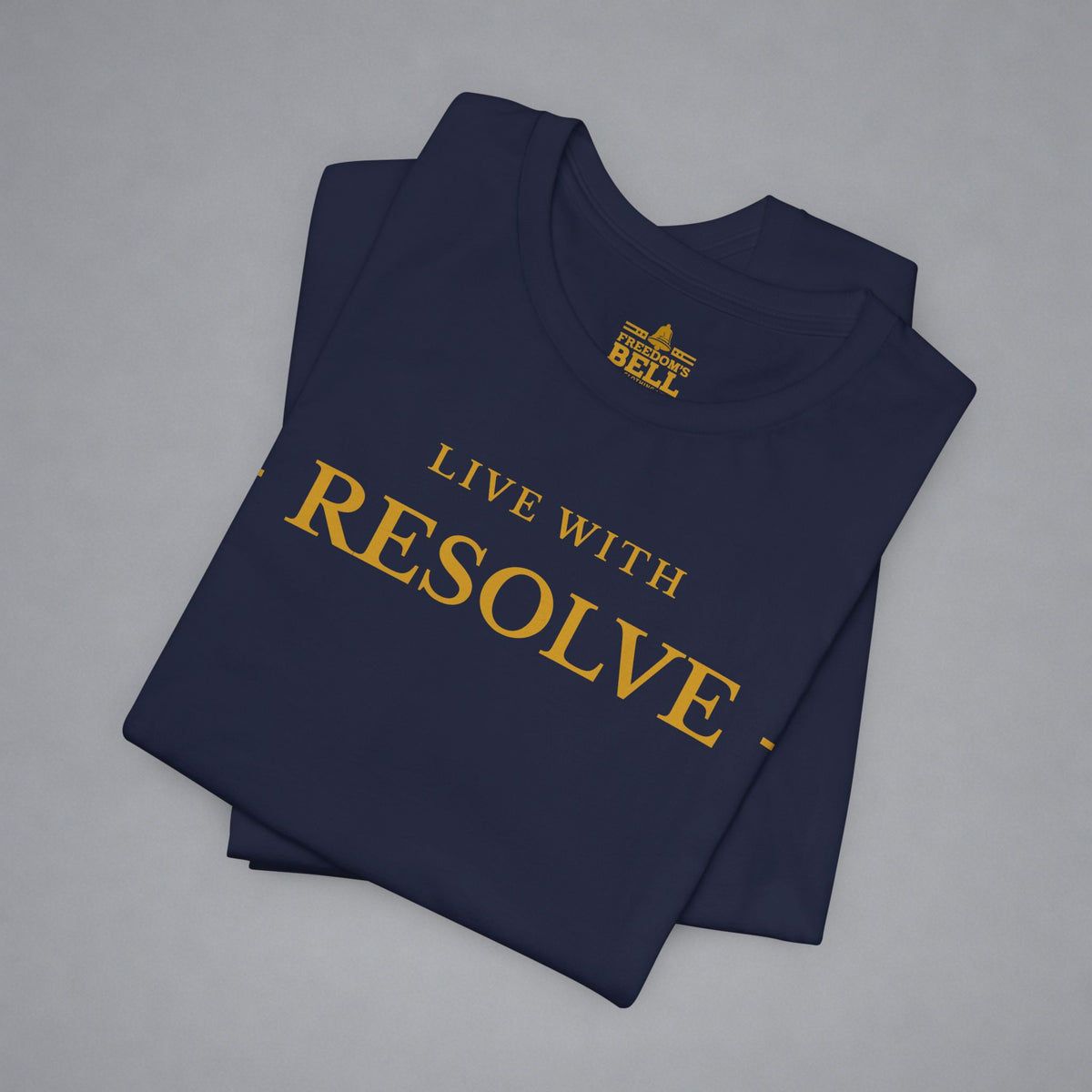 A folded navy blue t-shirt with gold text reading 'LIVE WITH RESOLVE' and a small 'BELLELL' logo printed inside the collar, displayed on a neutral gray background.