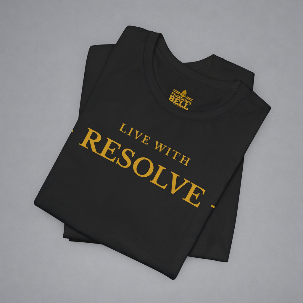 A folded black t-shirt with gold text reading 'LIVE WITH RESOLVE' and a small 'BELL' logo printed inside the collar, displayed on a neutral gray background.