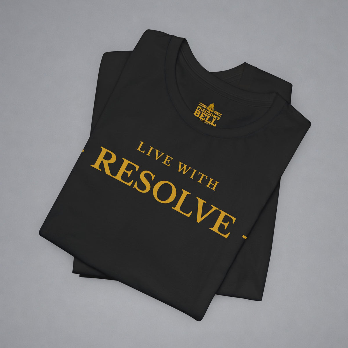 A folded black t-shirt with gold text reading 'LIVE WITH RESOLVE' and a small 'BELL' logo printed inside the collar, displayed on a neutral gray background.