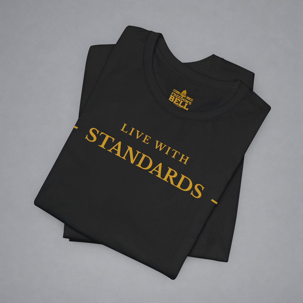 A folded black t-shirt with gold text reading 'LIVE WITH STANDARDS' and a gold 'Bell' logo printed inside the collar, displayed on a neutral gray background.