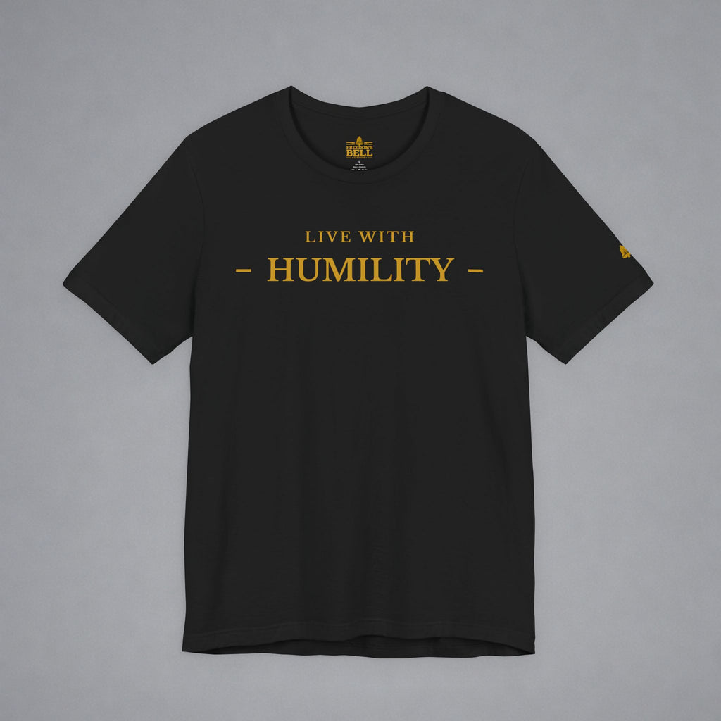 A black short-sleeve crewneck t-shirt with 'LIVE WITH - HUMILITY -' printed in gold across the chest, displayed flat against a neutral gray background.