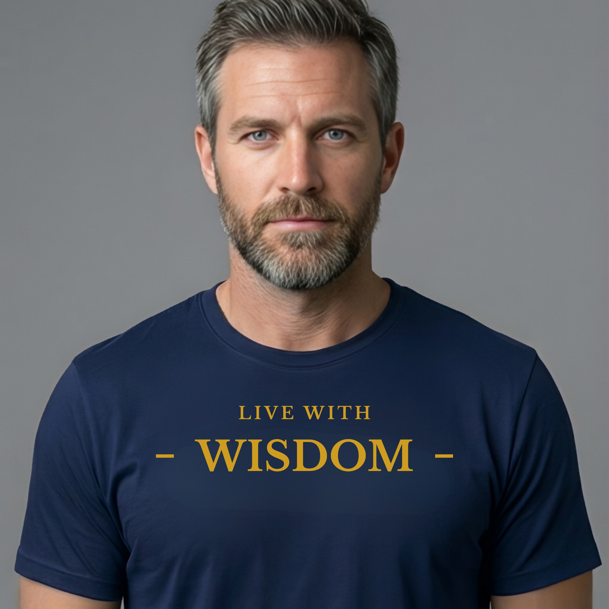 A man with short gray hair and a beard wearing a navy blue t-shirt with the text 'LIVE WITH - WISDOM -' printed in gold on the chest, set against a solid gray background.