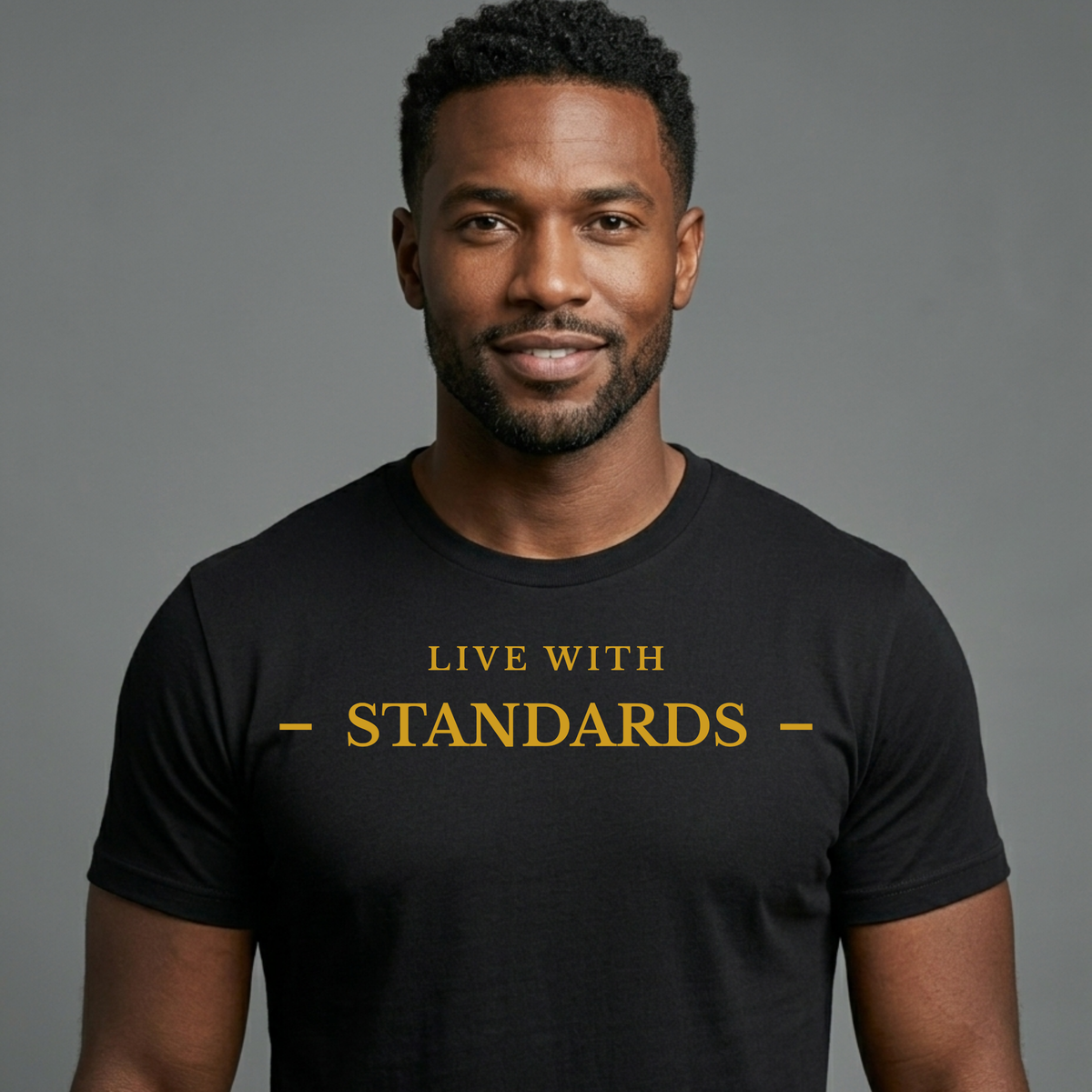 A man wearing a black crew-neck t-shirt with the text 'LIVE WITH STANDARDS' printed in gold across the chest, set against a solid gray studio background.