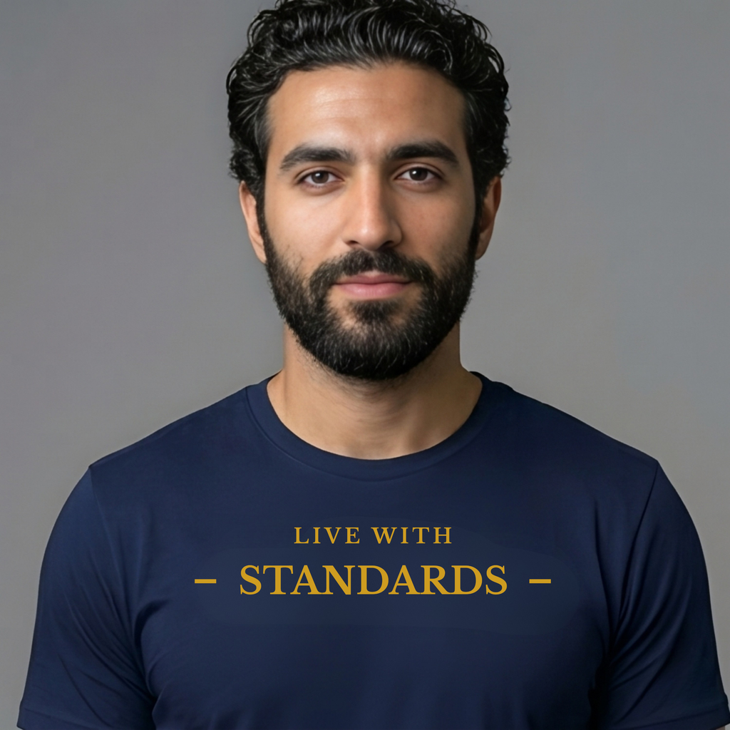 A man with a beard and dark hair wearing a navy blue t-shirt with the text 'LIVE WITH - STANDARDS -' printed in gold on the chest, set against a plain gray background.
