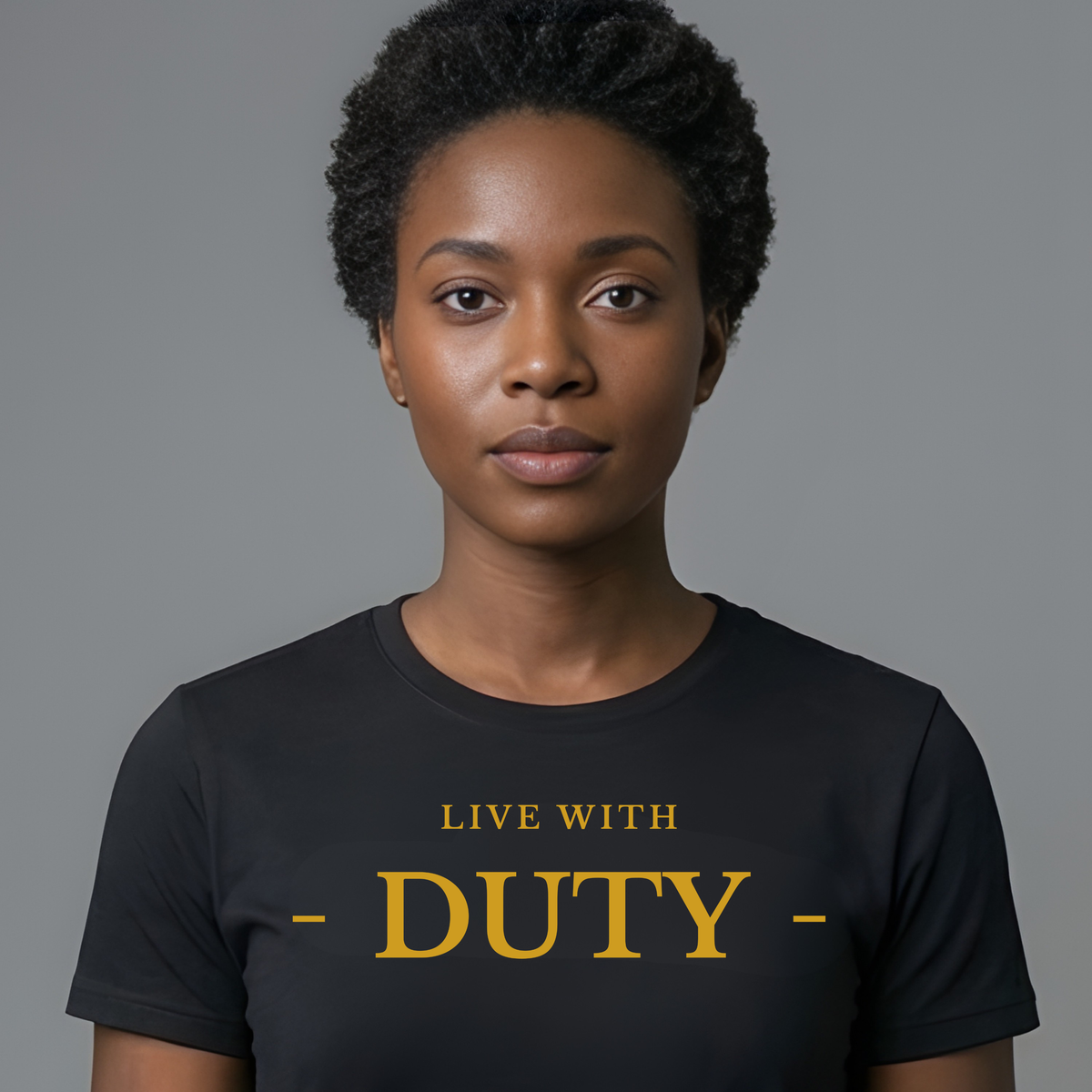A woman with short curly black hair wearing a black crewneck t-shirt with 'LIVE WITH - DUTY -' printed in gold lettering, set against a solid gray studio background.