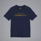 A navy blue crewneck t-shirt with 'LIVE WITH HUMILITY' printed in gold across the chest, displayed flat against a neutral gray background.